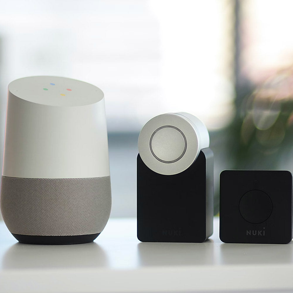 Smart home accessories: Google Home speaker with gray fabric base, silver Nuki Smart Lock, and black Nuki Door Sensor.