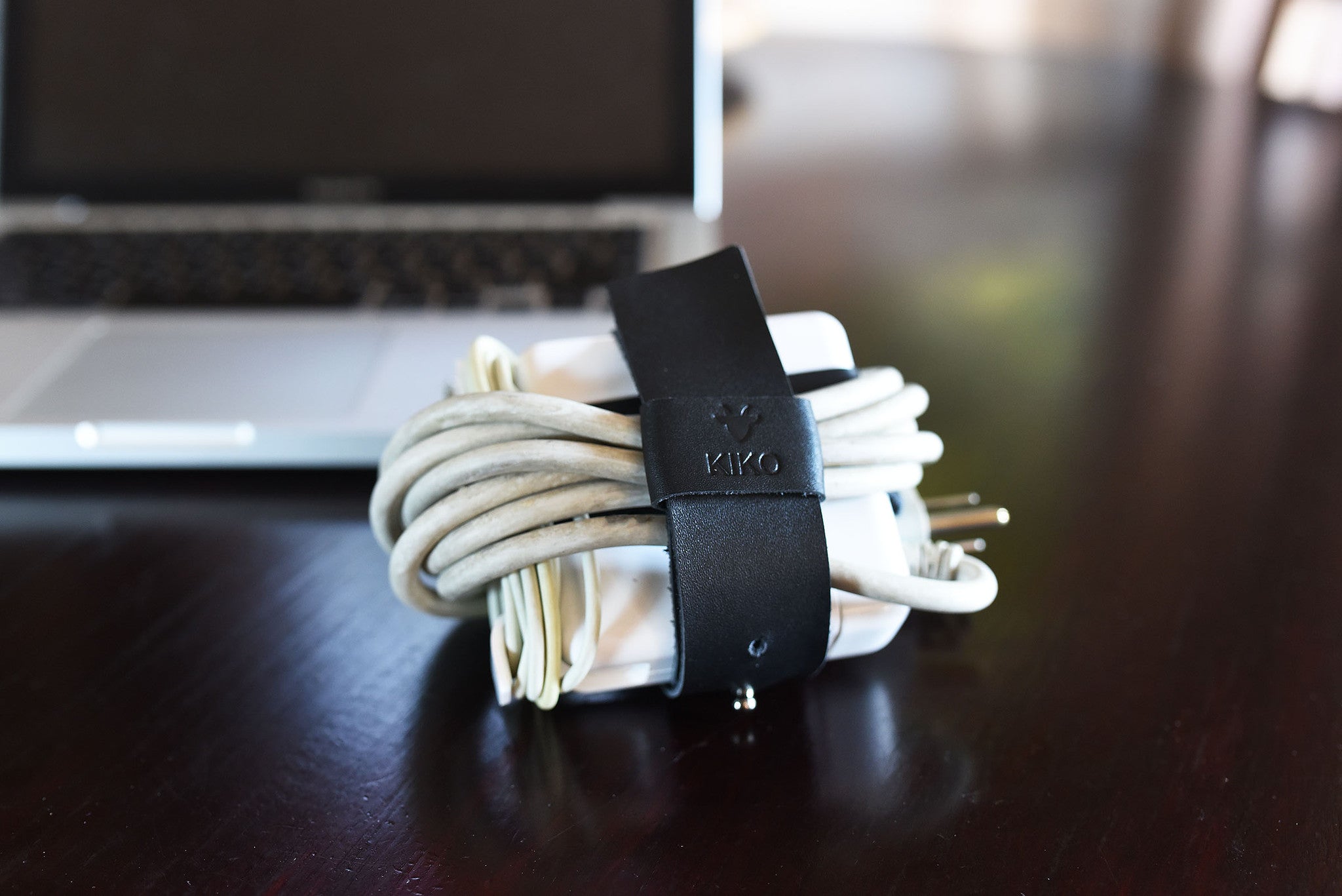 Black leather adjustable cable wrap from Kiko Leather, designed for organizing MacBook charger cords.