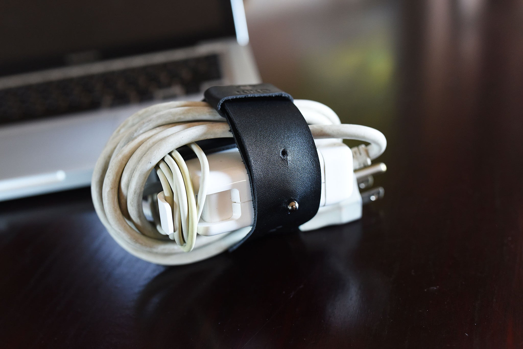 Adjustable black leather cord organizer for MacBook charger, featuring a sleek wrap design for effective cable management.